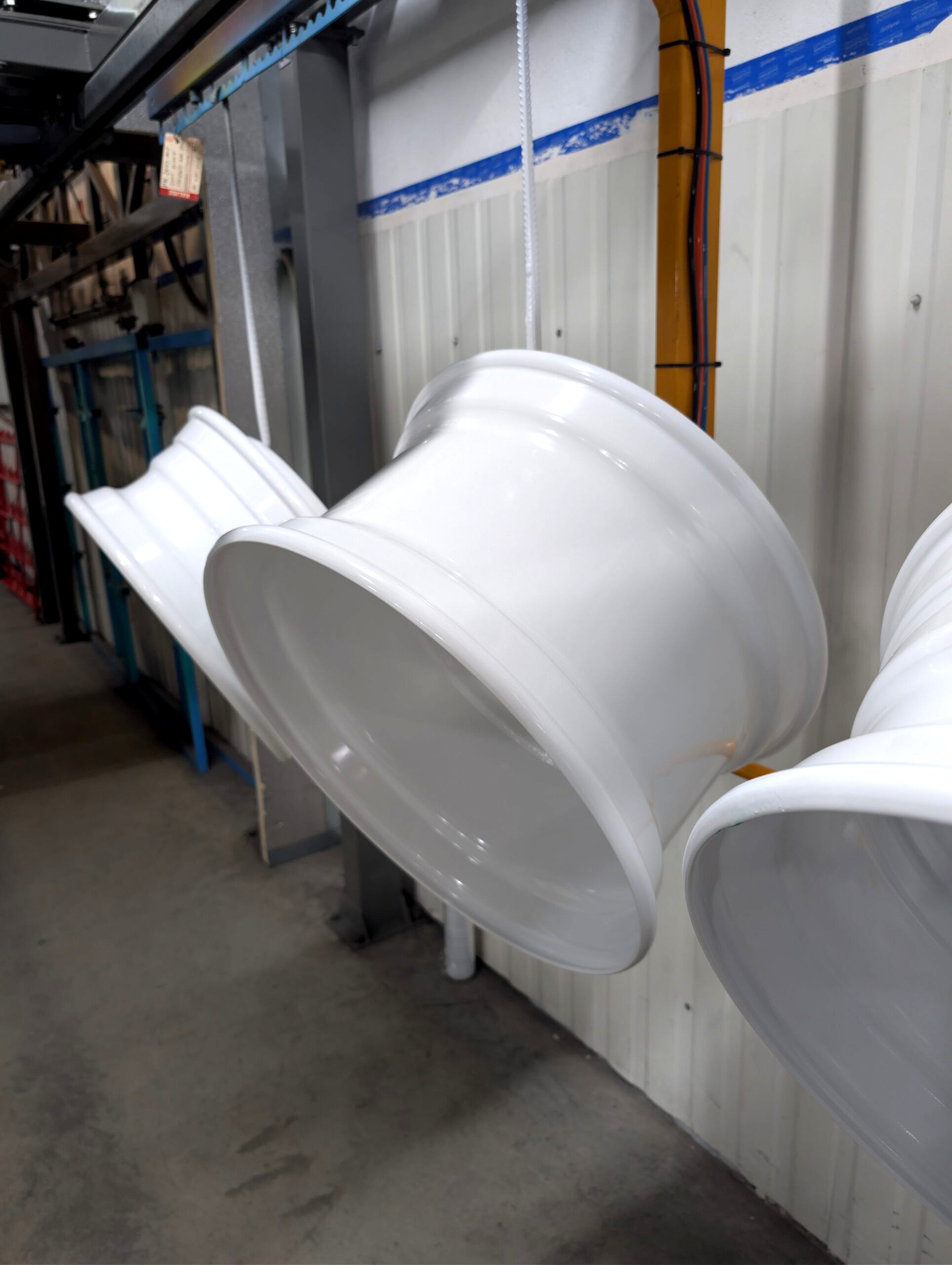 Felgi stalowe TIR zawieszone na linii lakierniczej po malowaniu proszkowym w kolorze białym połysk RAL 9010 – lakiernia Koczargi